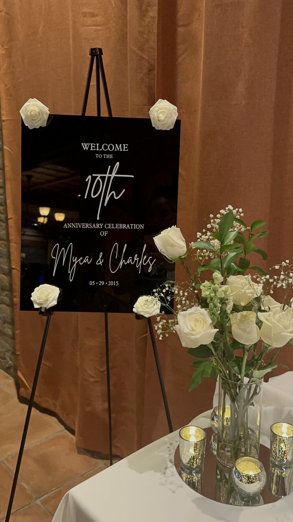 Welcome to the 10th Anniversary Celebration of Myca and Charles, black welcome sign on an easel with white roses