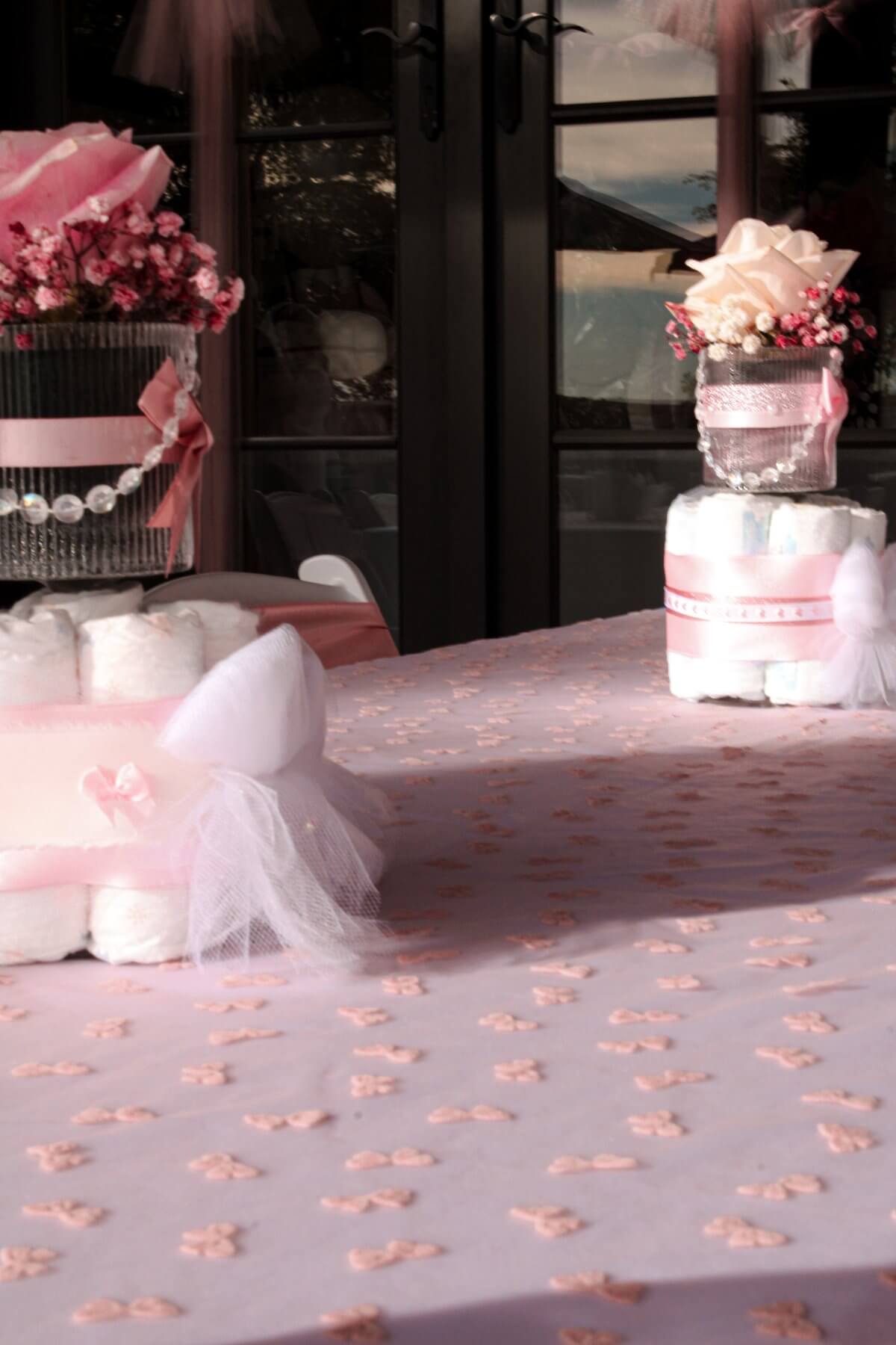 Pink rose and baby's breath centerpieces atop diaper cakes, styled on a bow-pattern tablecloth