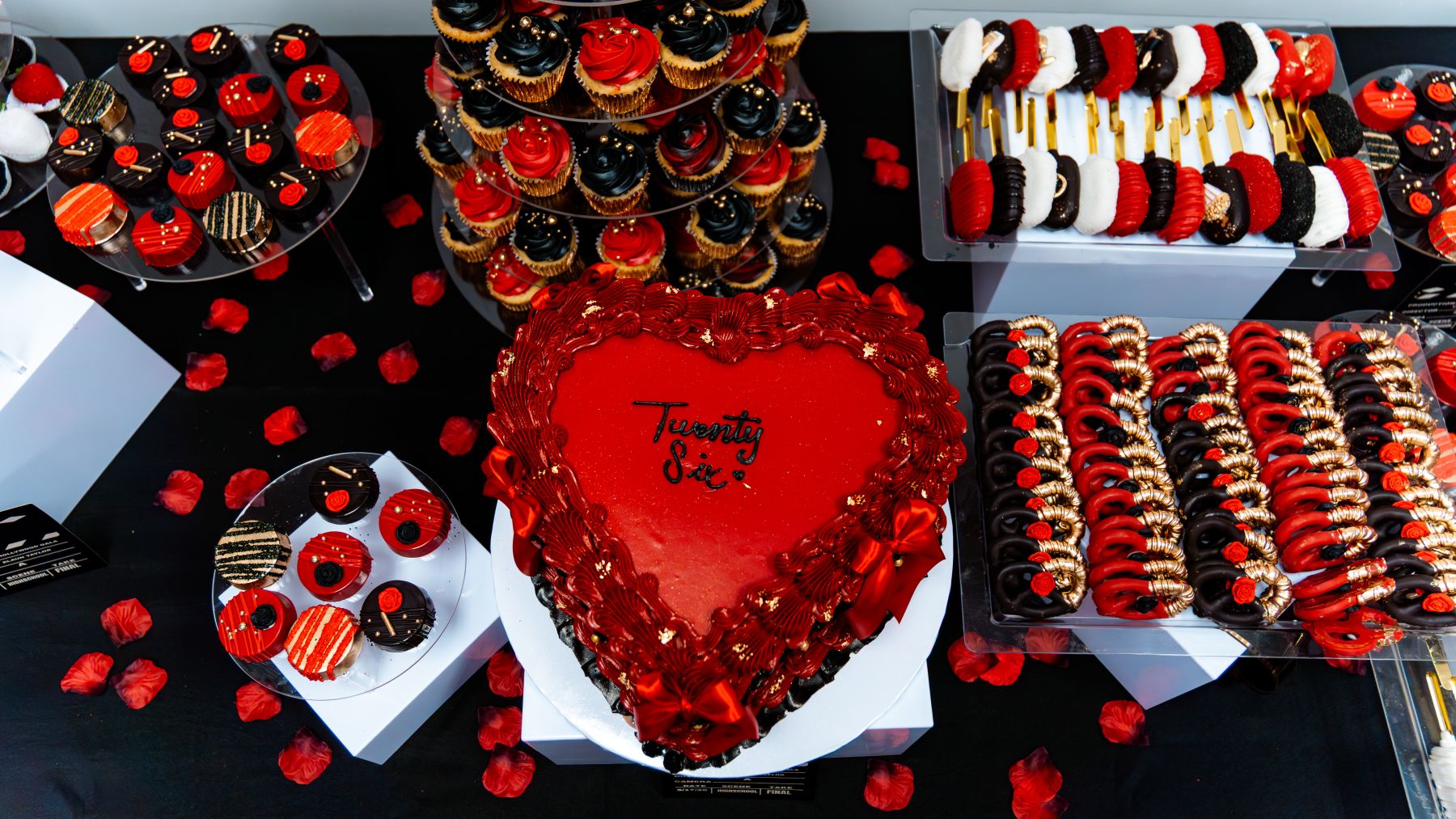 Hollywood gala dessert table with a red heart cake, cupcakes, and chocolate-dipped strawberries